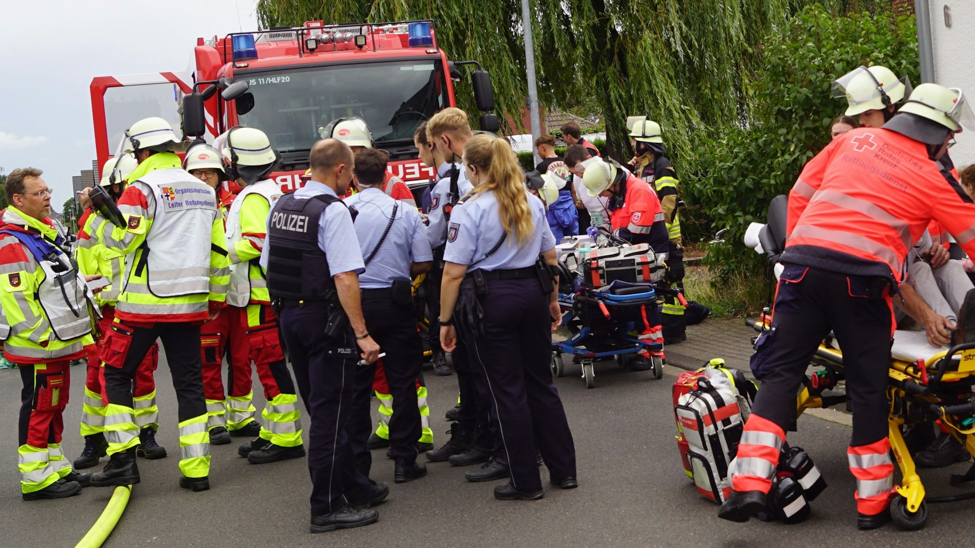 Das Bild zeigt mehrere Beamte und Einsatzkräfte. Rechts im Bild wird ein Mann behandelt.