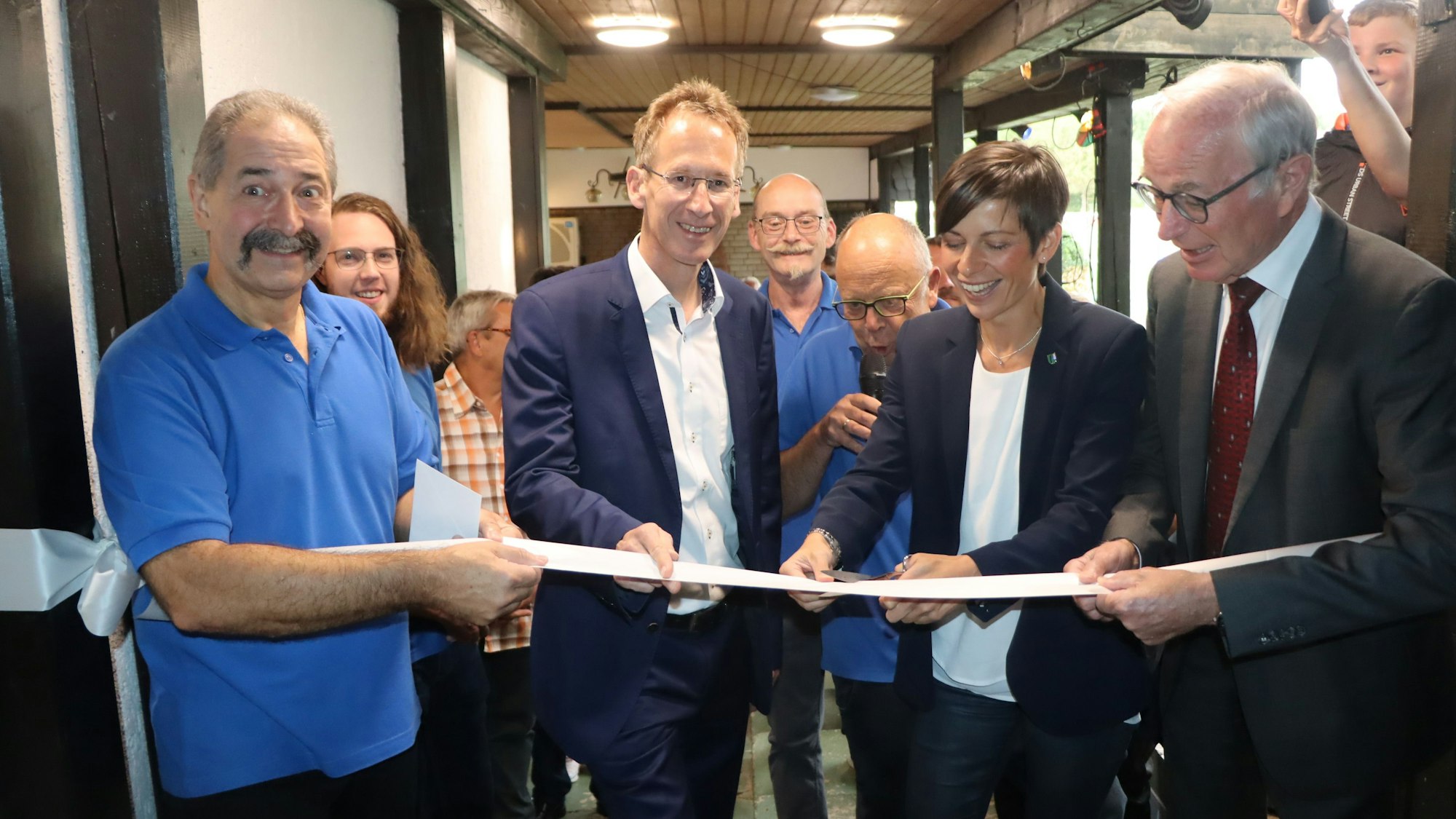 Drei Männer und eine Frau schneiden ein Band durch, es ist eine symbolische Geste.