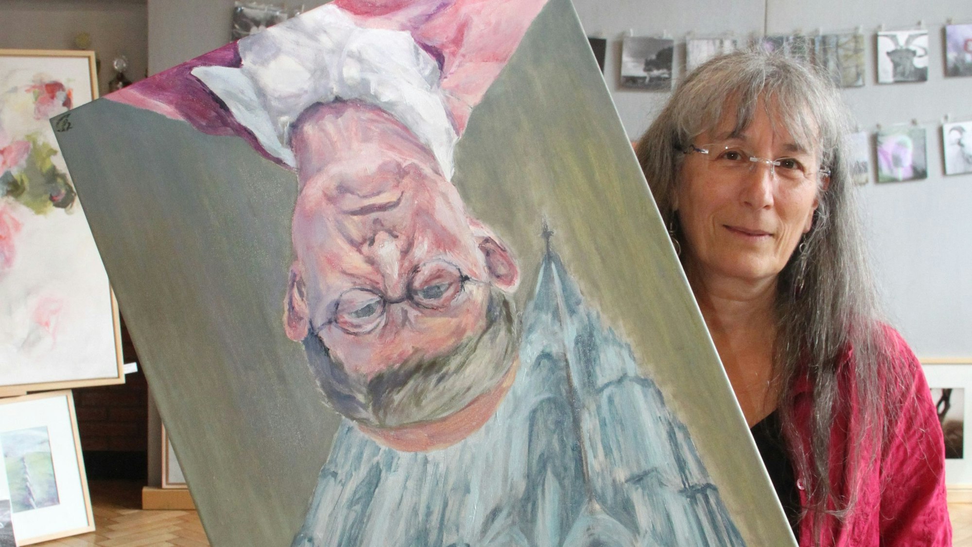 Die Künstlerin Yvonne Delisle zeigt ihr Werk „Der Himmel über Köln - so oder so“. Es zeigt den Kölner Kardinal Rainer Maria Woelki und dem Dom: Eins von beidem steht bei der Hängung Kopf.