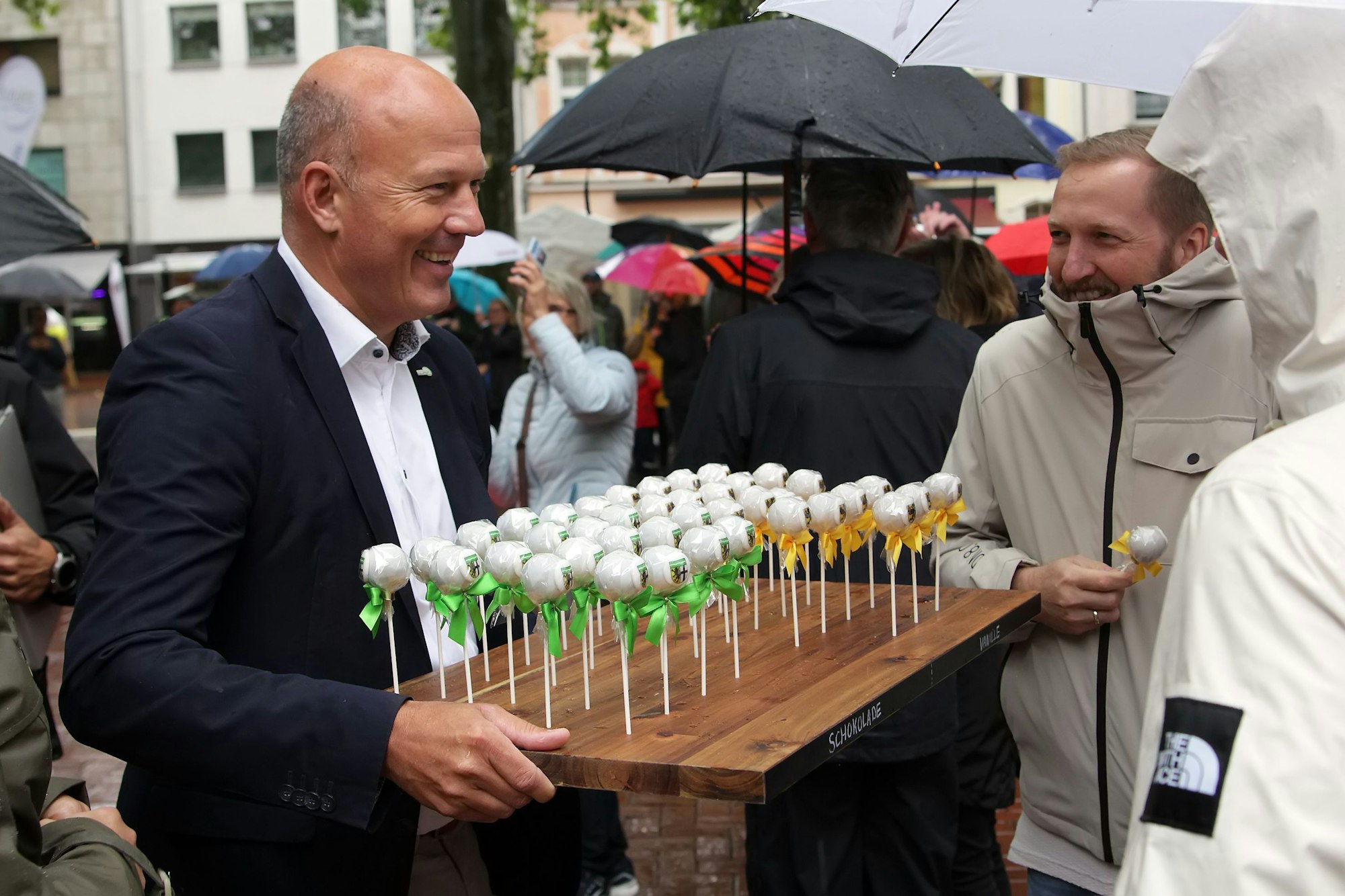 Ein Mann bietet anderen kleine Kuchen am Stiel an.