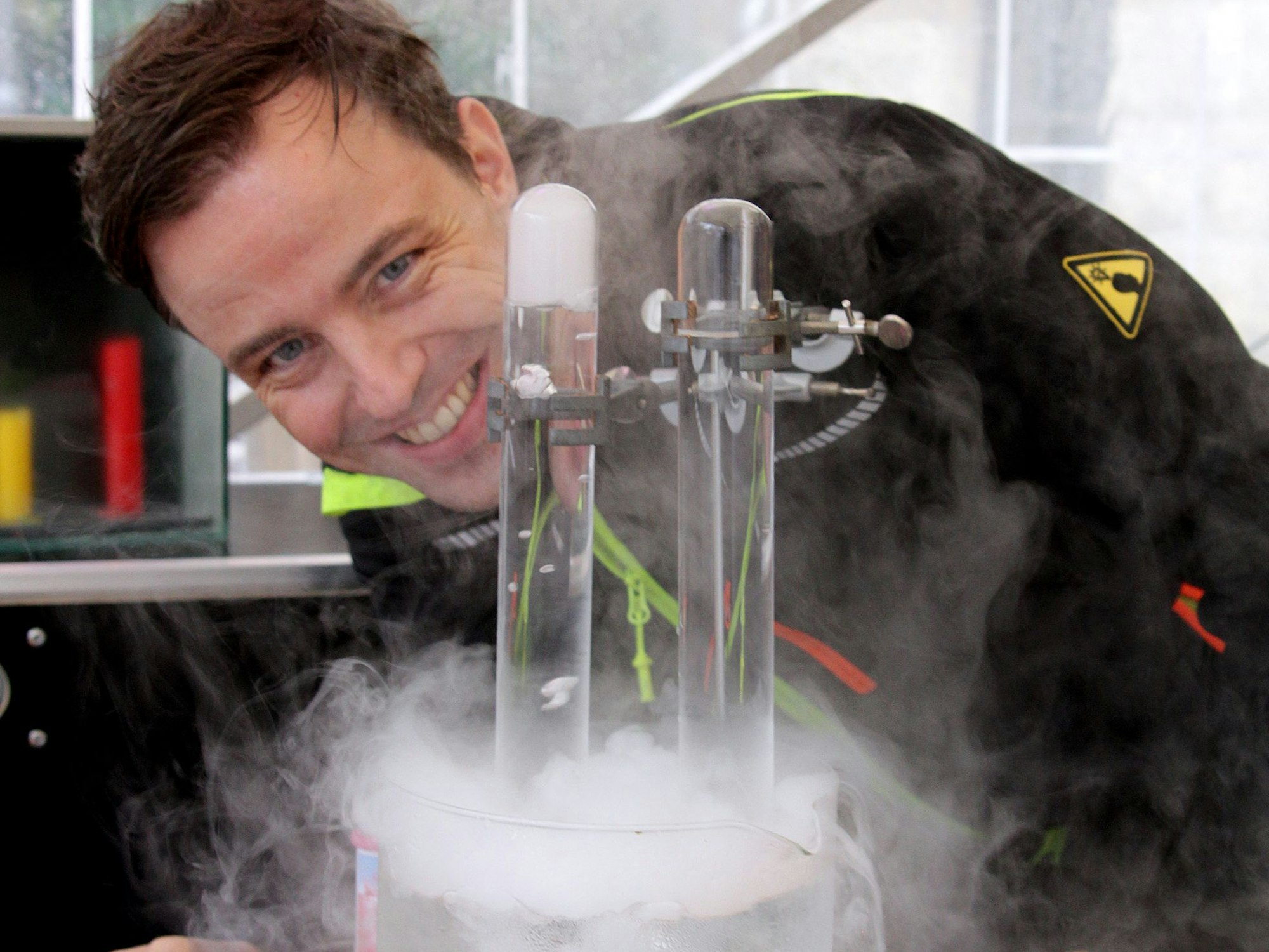 Ein Man beugt sich lächelnd über einen Glaszylinder, aus dem Dämpfe steigen.