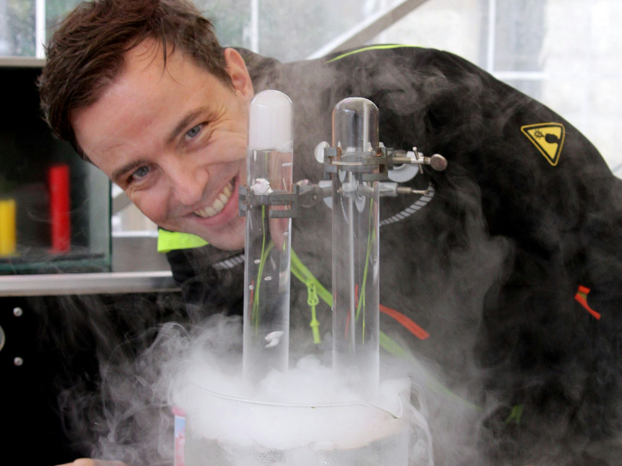 Ein Man beugt sich lächelnd über einen Glaszylinder, aus dem Dämpfe steigen.