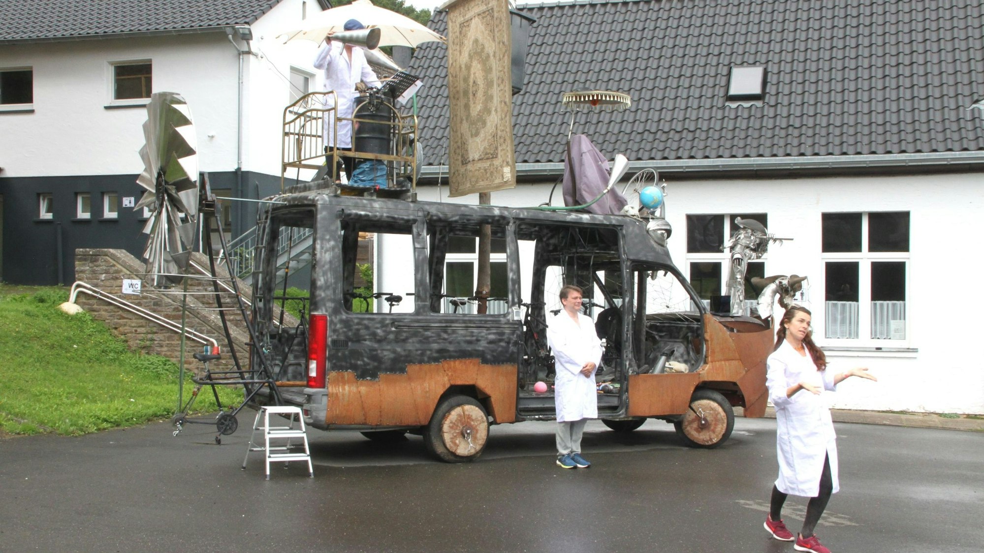 Die futuristische Klima-Galeere des Künstlers Peter Ratz steht auf einem Platz. Zwei Künstler in weißen Kitteln stehen davor, einer darauf.