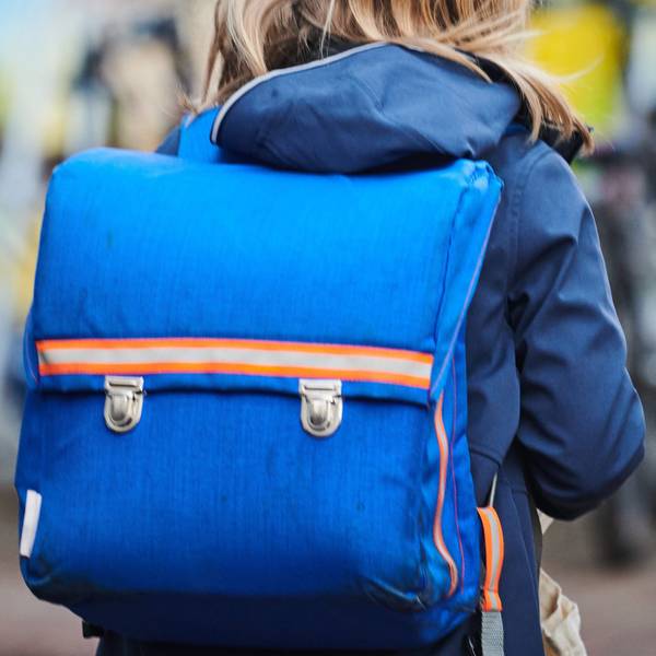 Ein Schüler steht mit Schulranzen nahe einer Grundschule.
