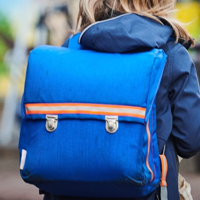 Ein Schüler steht mit Schulranzen nahe einer Grundschule.