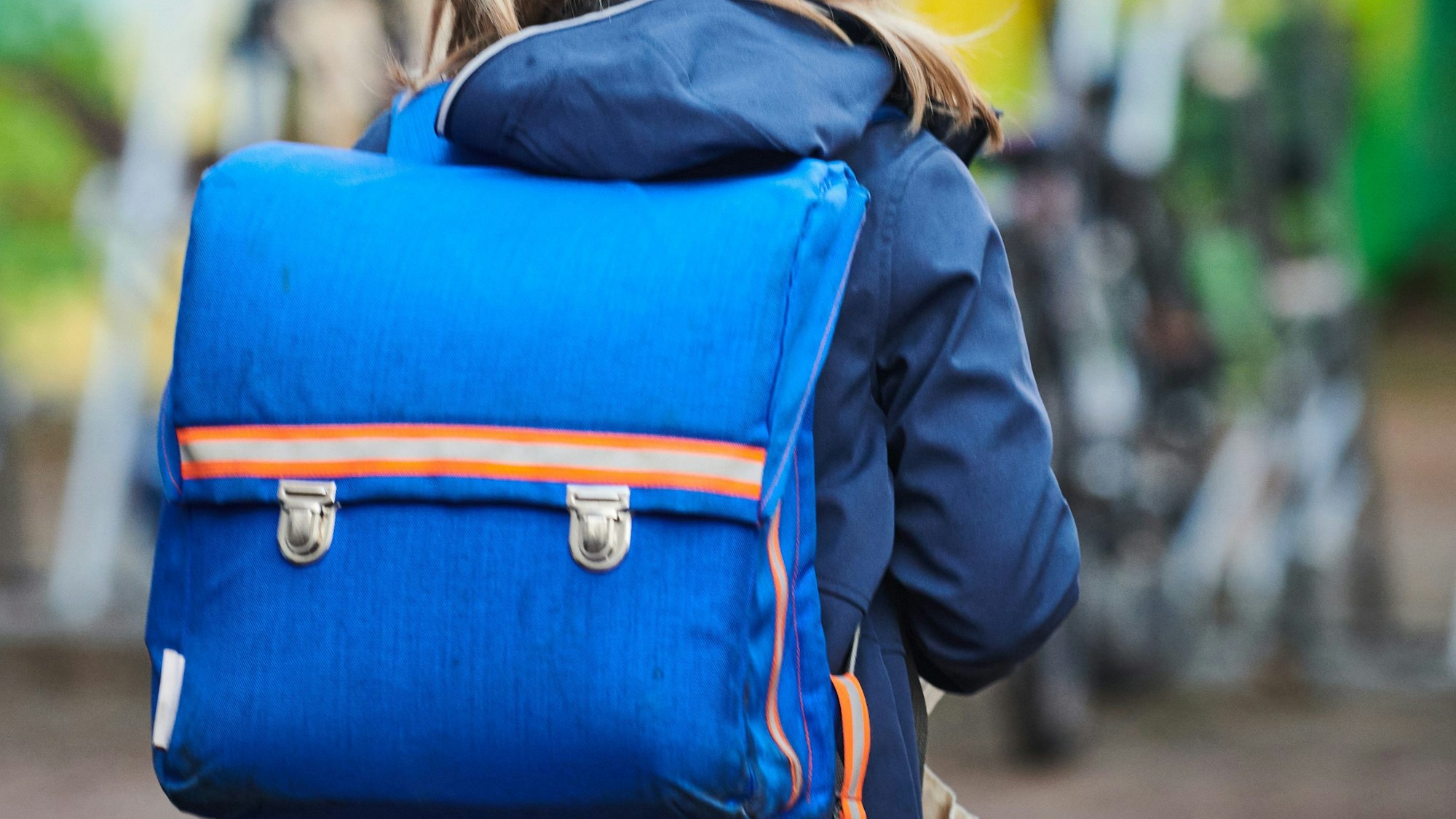 Ein Schüler steht mit Schulranzen nahe einer Grundschule.