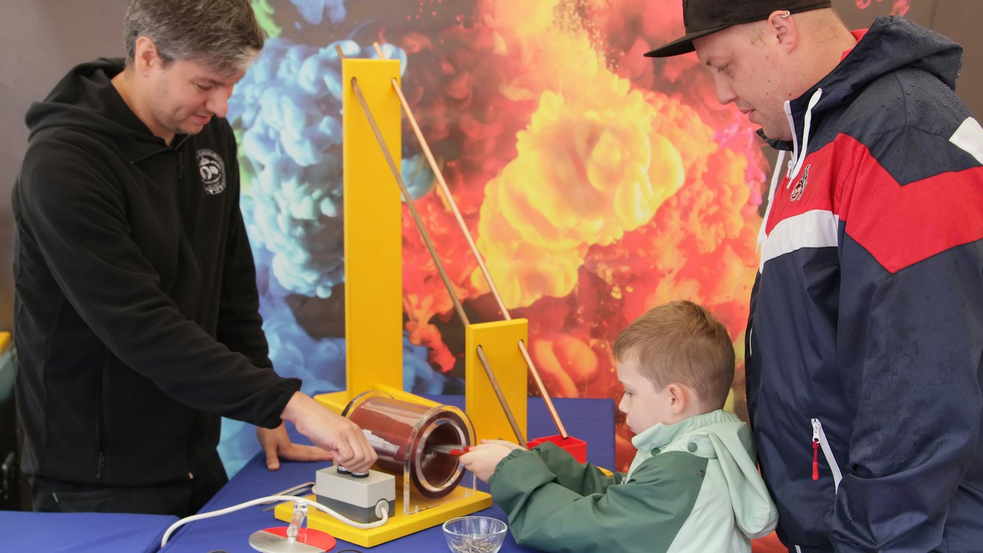 Zwei Männer einem Kind zu, das mit einer Maschine experimentiert.