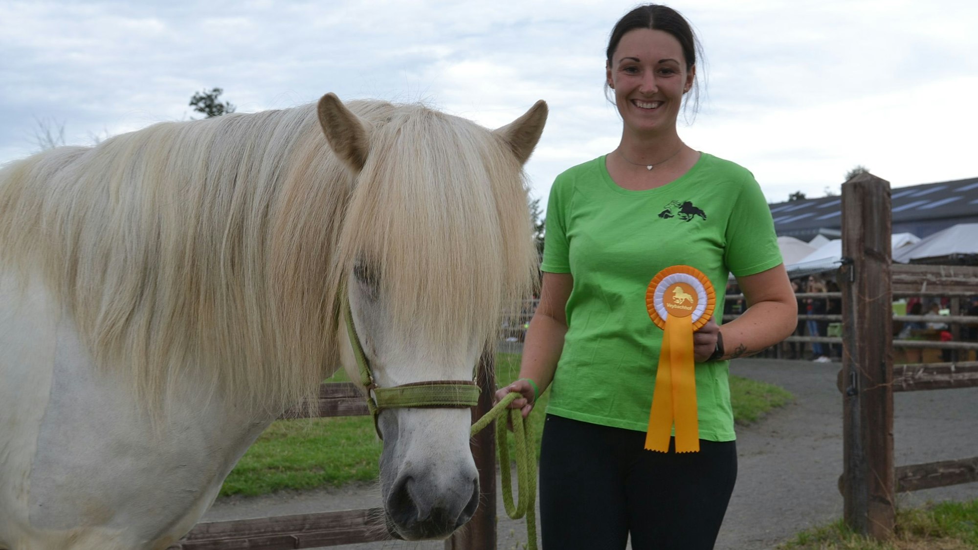 Das Bild zeigt die Reiterin Jasmin Pesch und die 14-jährige Island-Stute Kvikur. Die reiterin hält eine Siegerschleife in der Hand.