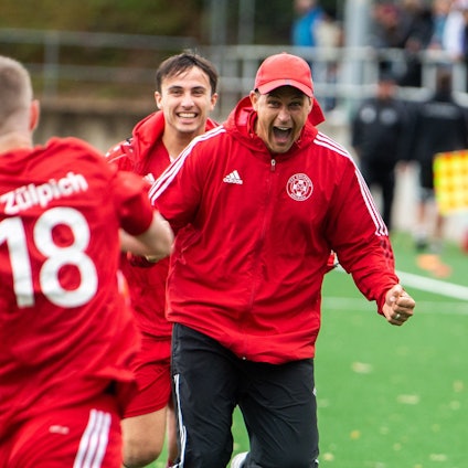 Das Bild zeigt Zülpichs Trainer David Sasse, der auf Torschütze Dominik Spies zuläuft, nachdem dieser ein Tor erzielt hat.