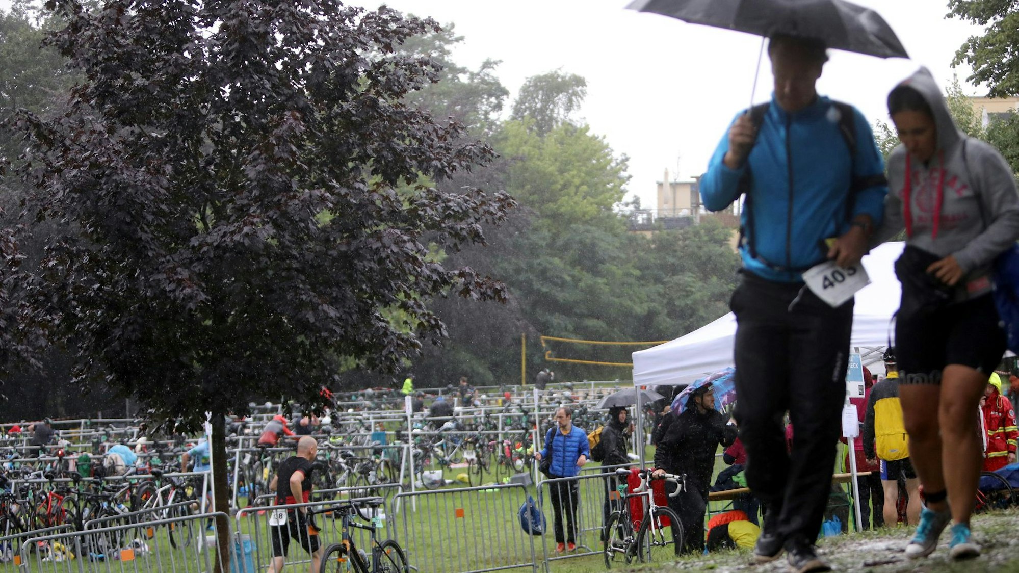 Menschen mit Regenschirm laufen über eine matschige Wiese.