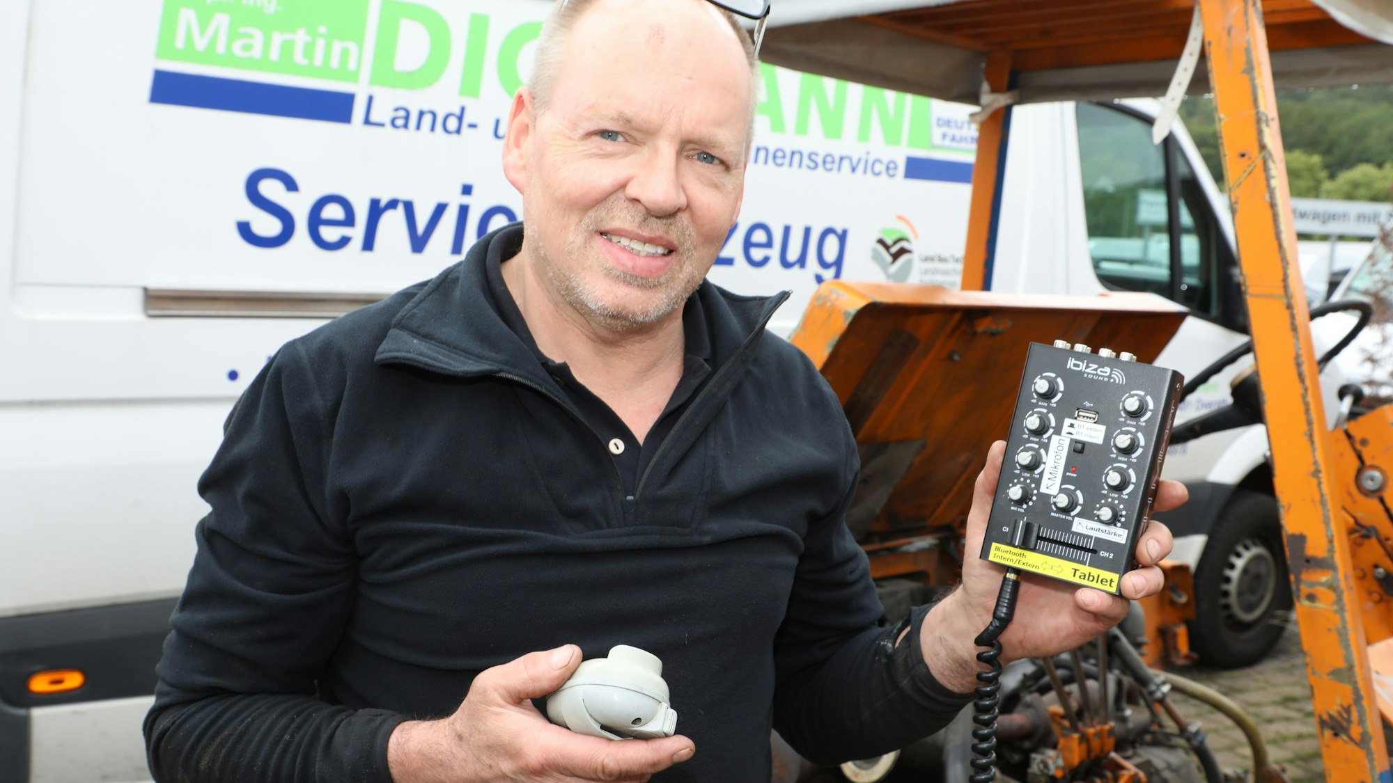 Ein Mann hält ein kleines Mischpult mit Mikrofon am Spiralkabel in die Höhe.