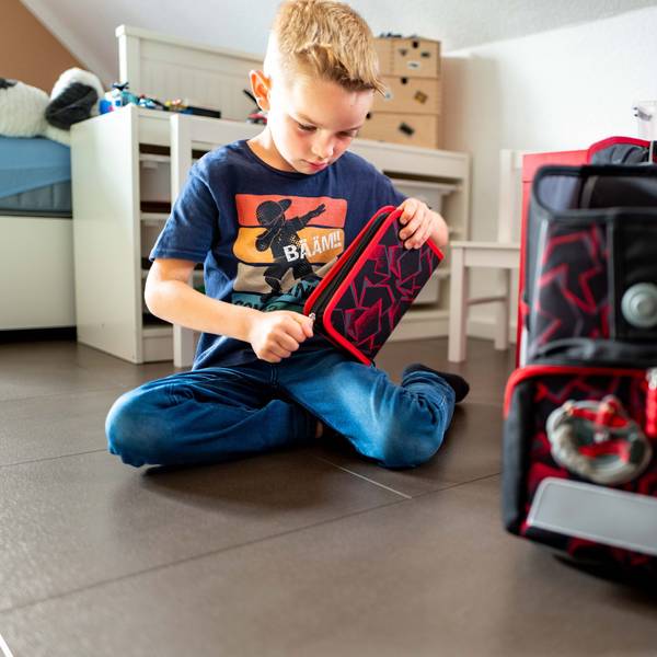 Grundschüler Lion Preiser sitzt auf dem Boden und öffnet sein neues Mäppchen.