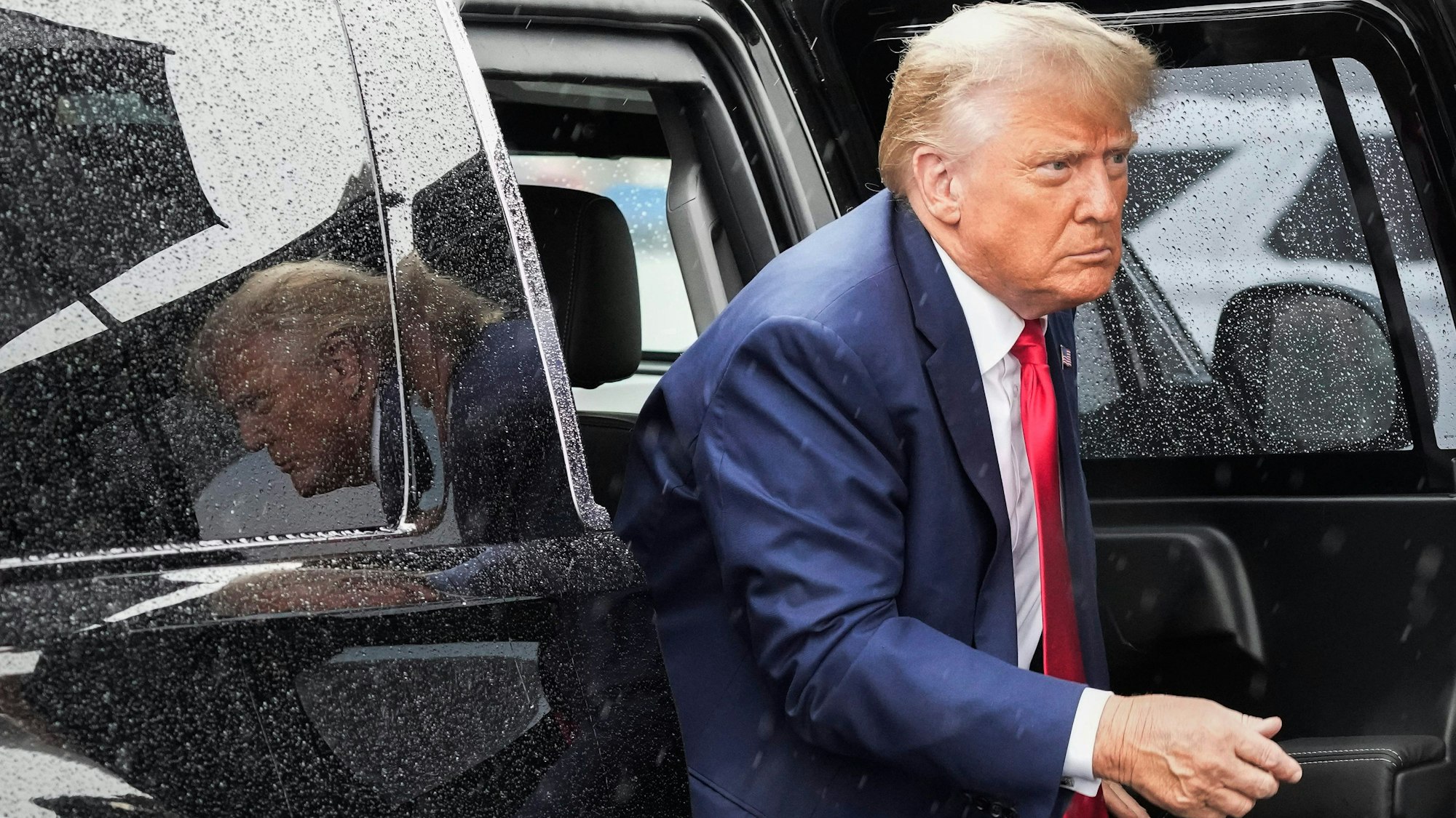 Der ehemalige US-Präsident Donald Trump steigt aus einem verregneten, schwarzen Auto.