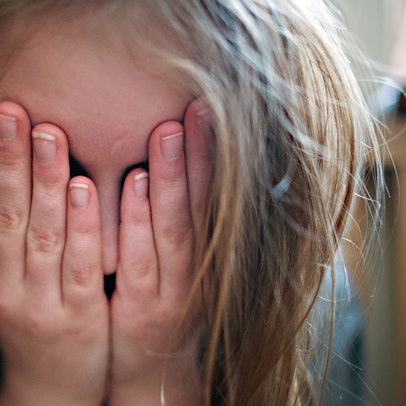 Ein junges Mädchen hält sich die Hände vor ihr Gesicht.