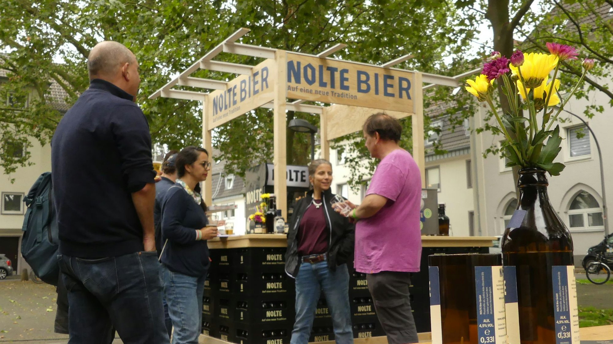 Einige Personen stehen an einer hölzernen Theke unter freiem Himmel.