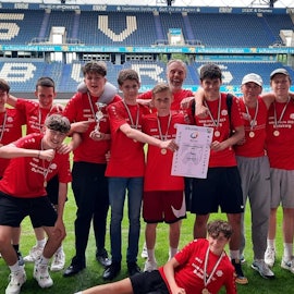 Eine Reihe von Schülerinnen und Schülern in Trikots vor der Tribüne eines Stadions.