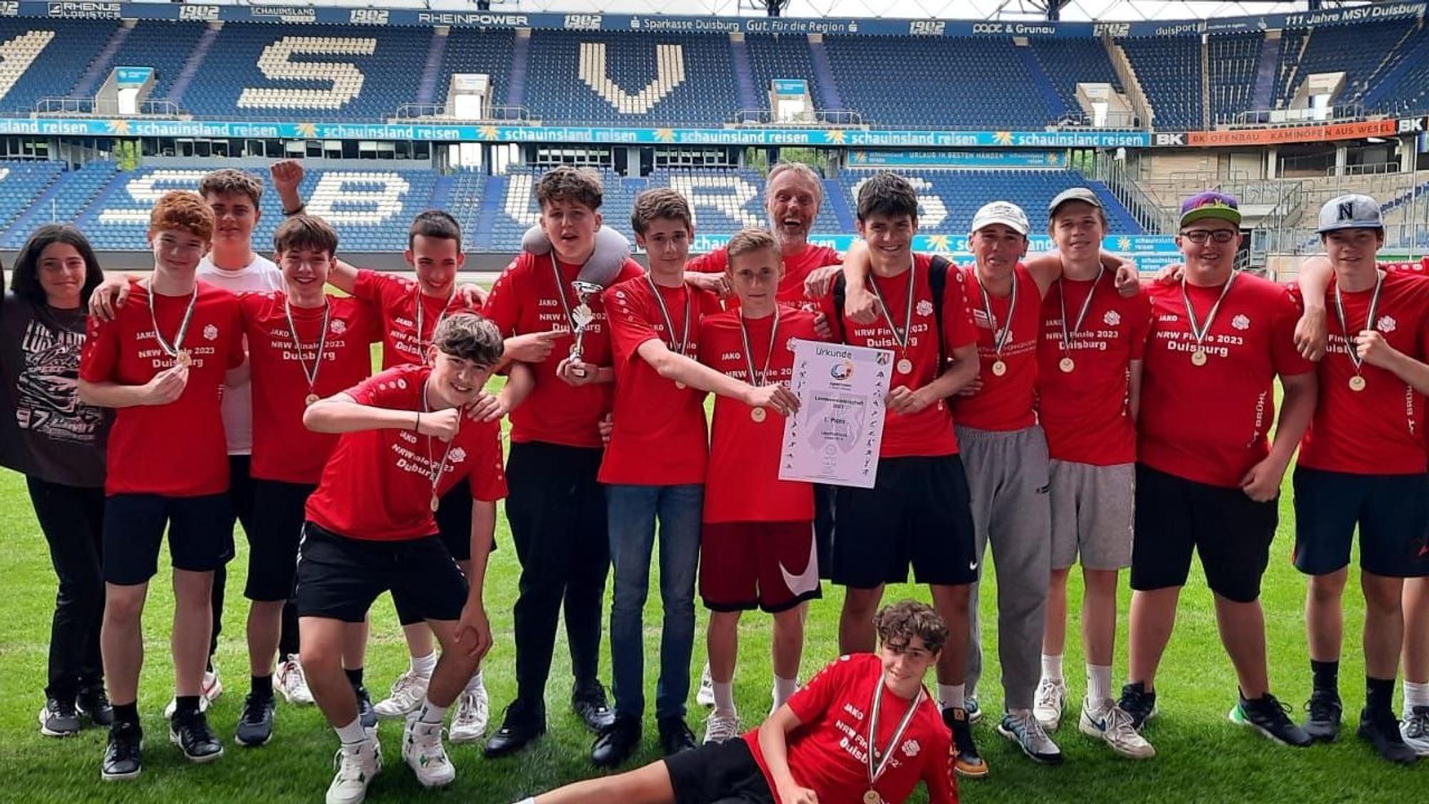 Eine Reihe von Schülerinnen und Schülern in Trikots vor der Tribüne eines Stadions.