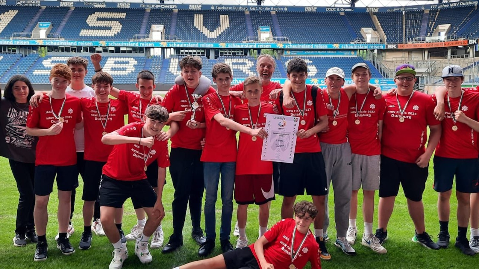 Eine Reihe von Schülerinnen und Schülern in Trikots vor der Tribüne eines Stadions.