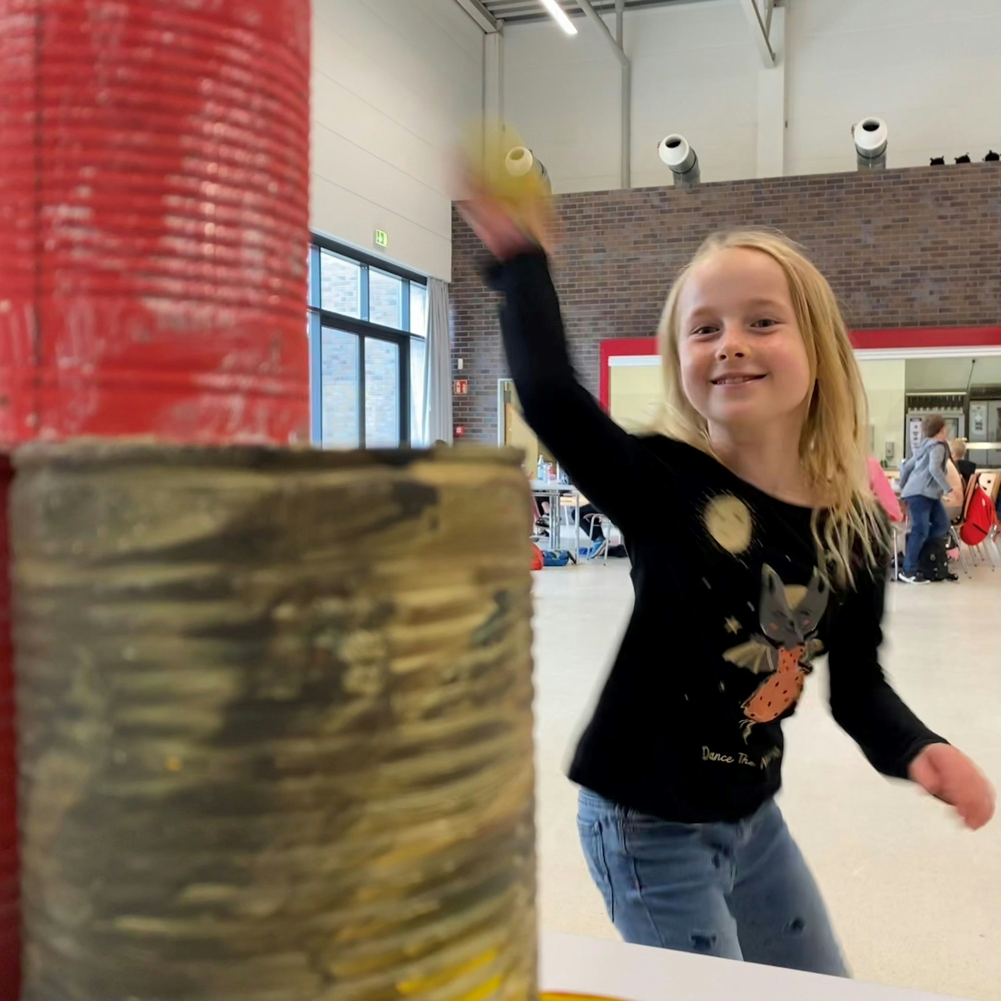 Kiyana steht vor einer Pyramide angemalter Blechdosen und zielt mit einem Ball.