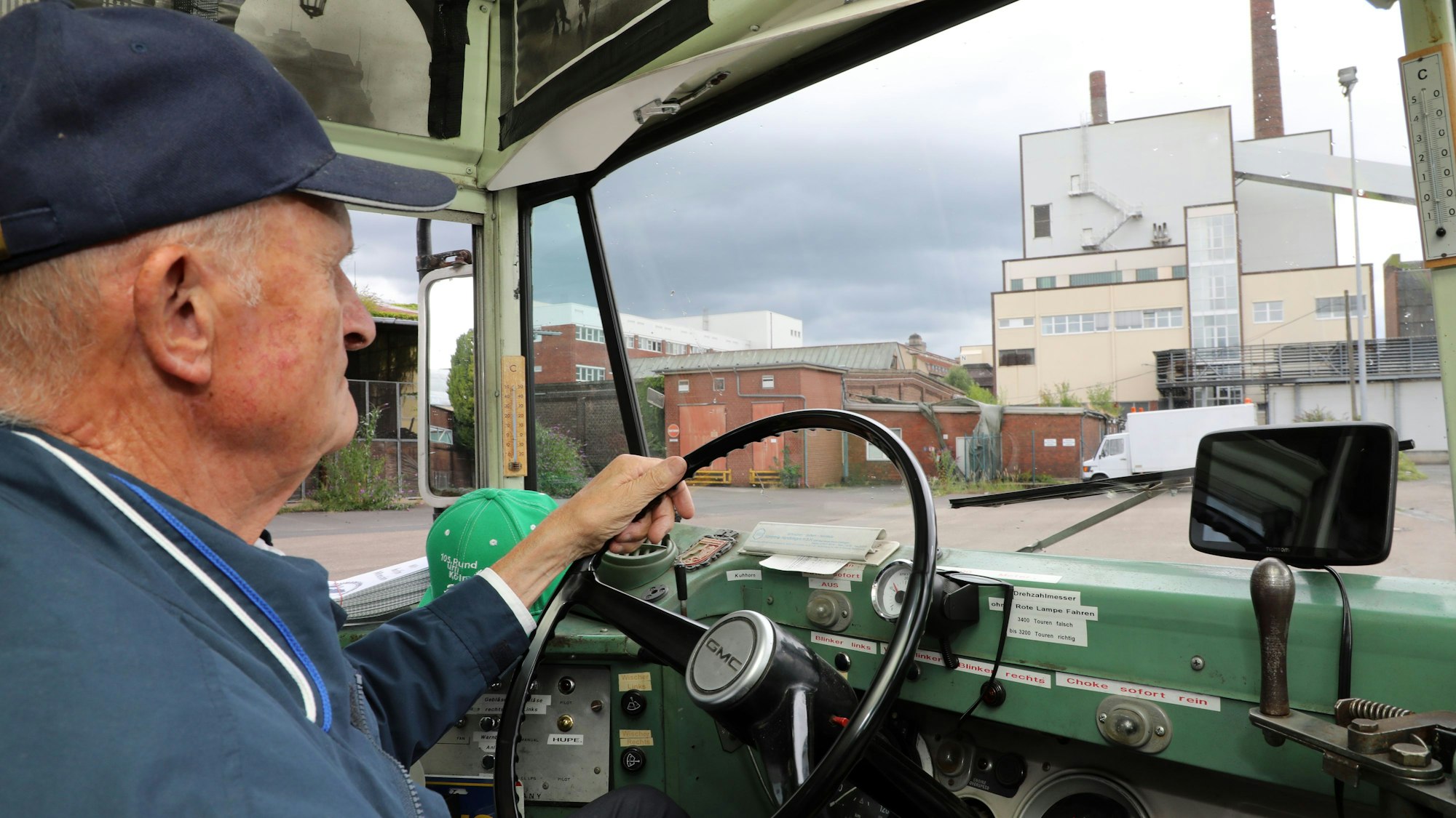 Ein Mann sitzt am Steuer eines historischen amerikanischen Schulbusses und fährt über ein ehemaliges Werksgelände.