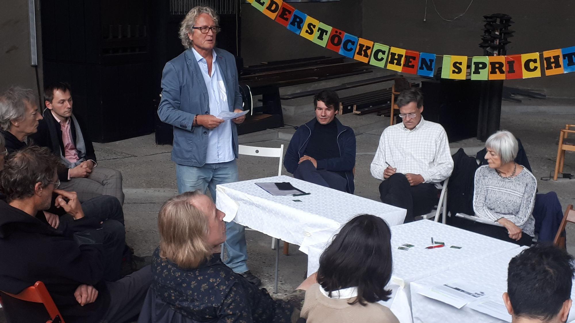 Ein Mann steht vor einem Tisch, an dem Gäste sitzen.