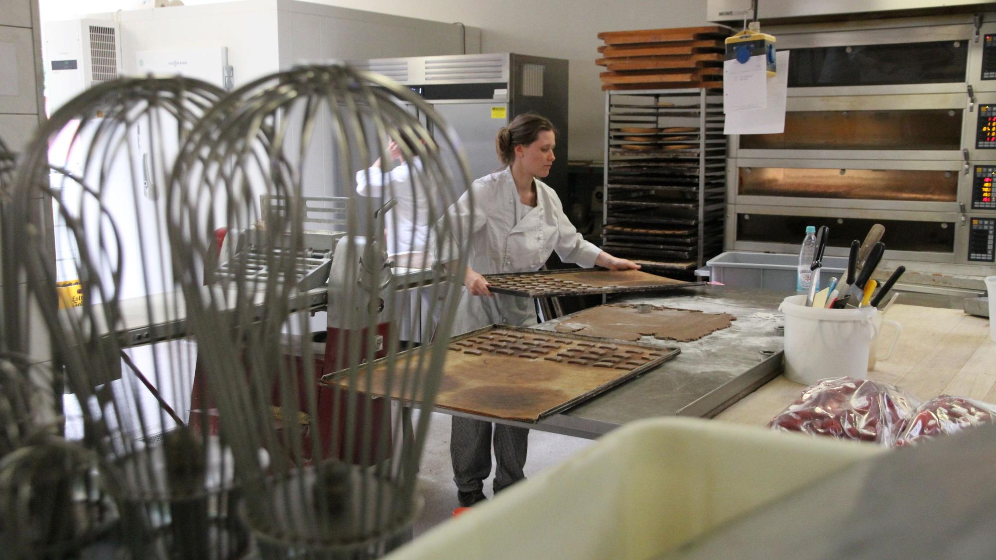 Eine junge Frau arbeitet in der Backstube. Sie legt ein Tablett auf einen Metallarbeitstisch.