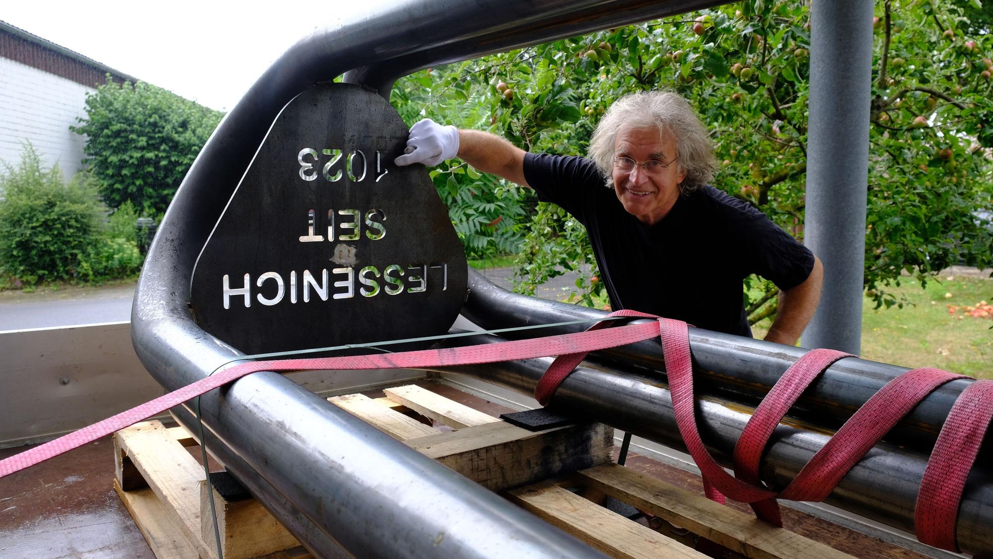 Neben einer Gedenkstele mit der Aufschrift „Lessenich seit 1023“ steht der Künstler Karl Hubert Schmitt. Er trägt einen weißen Handschuh und deutet auf die Inschrift.