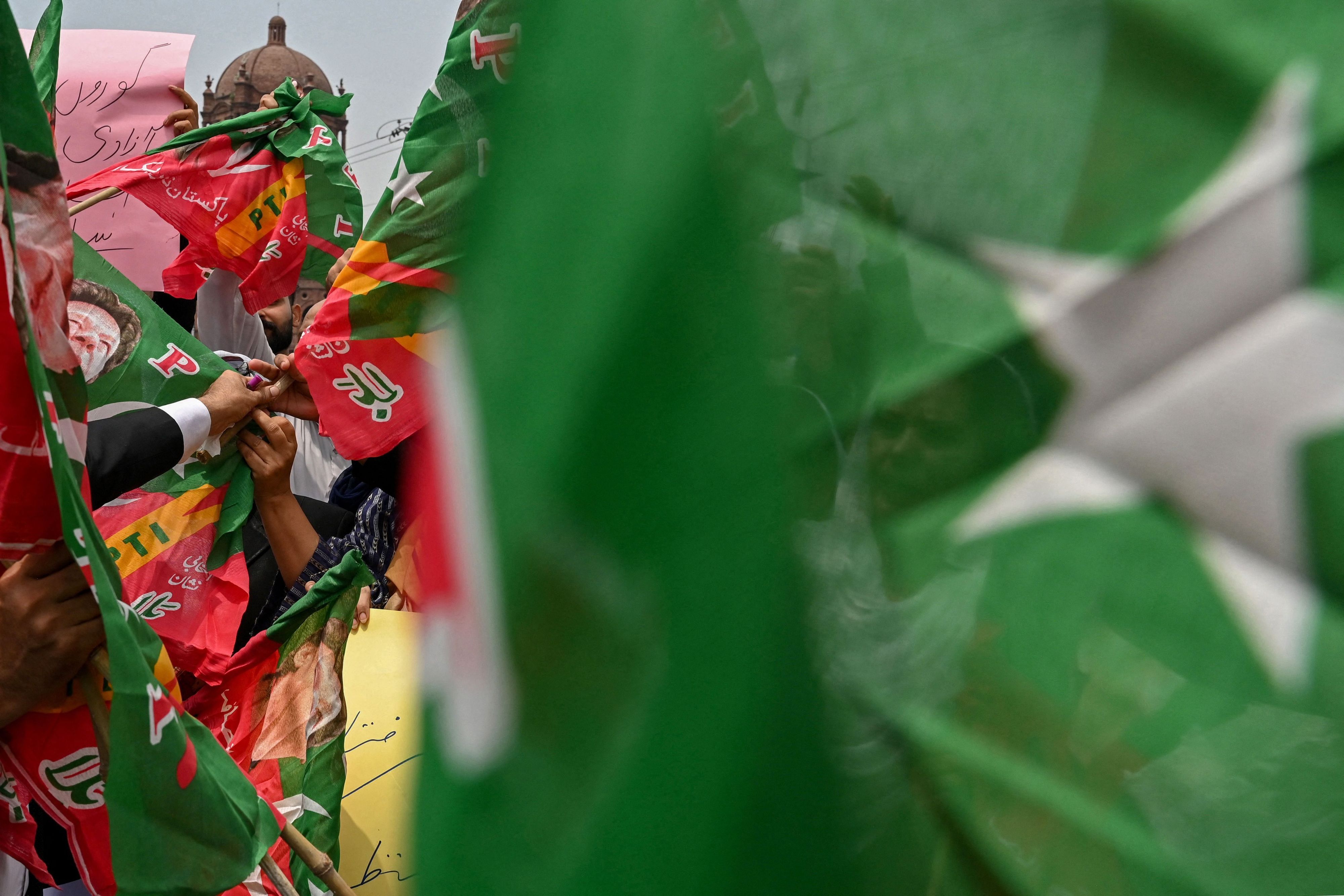 Menschen halten Banner hinter einer unscharfen pakistanischen Flagge hoch. (Symbolbild)