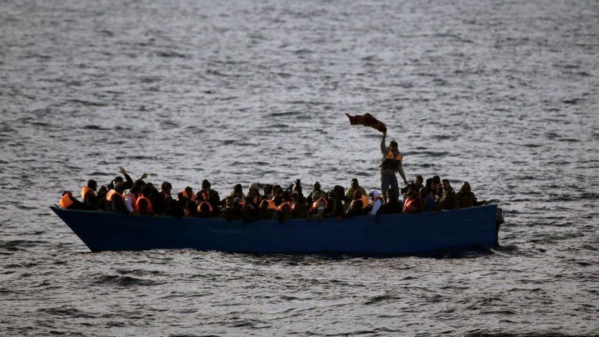 Geflüchtete aus Afrika rufen auf dem Mittelmeer in einem Boot um Hilfe.