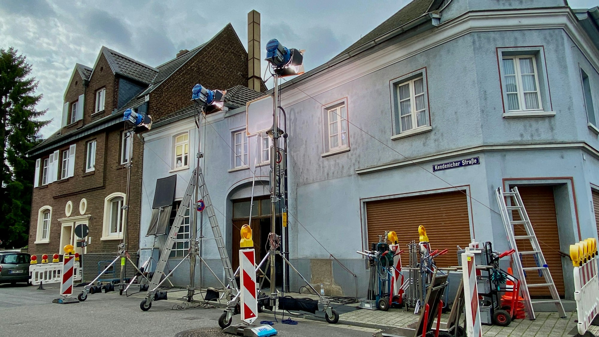 Das Bild zeigt ein Wohnhaus, an dem für die Dreharbeiten große Scheinwerfer aufgebaut und weitere Filmausrüstung abgestellt wurden.
