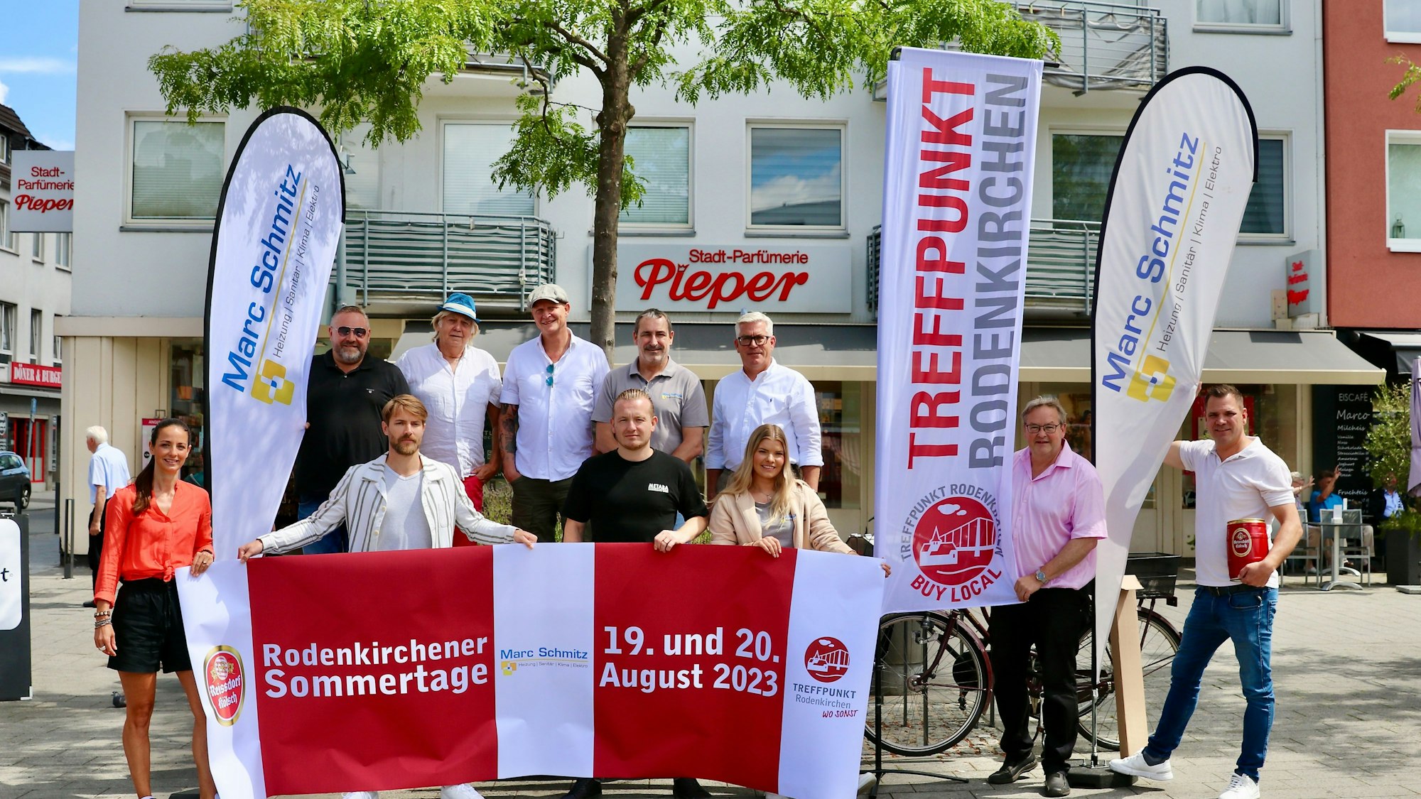 Eine Gruppe von Männern und Frauen präsentiert Werbefahnen auf einem Marktplatz.