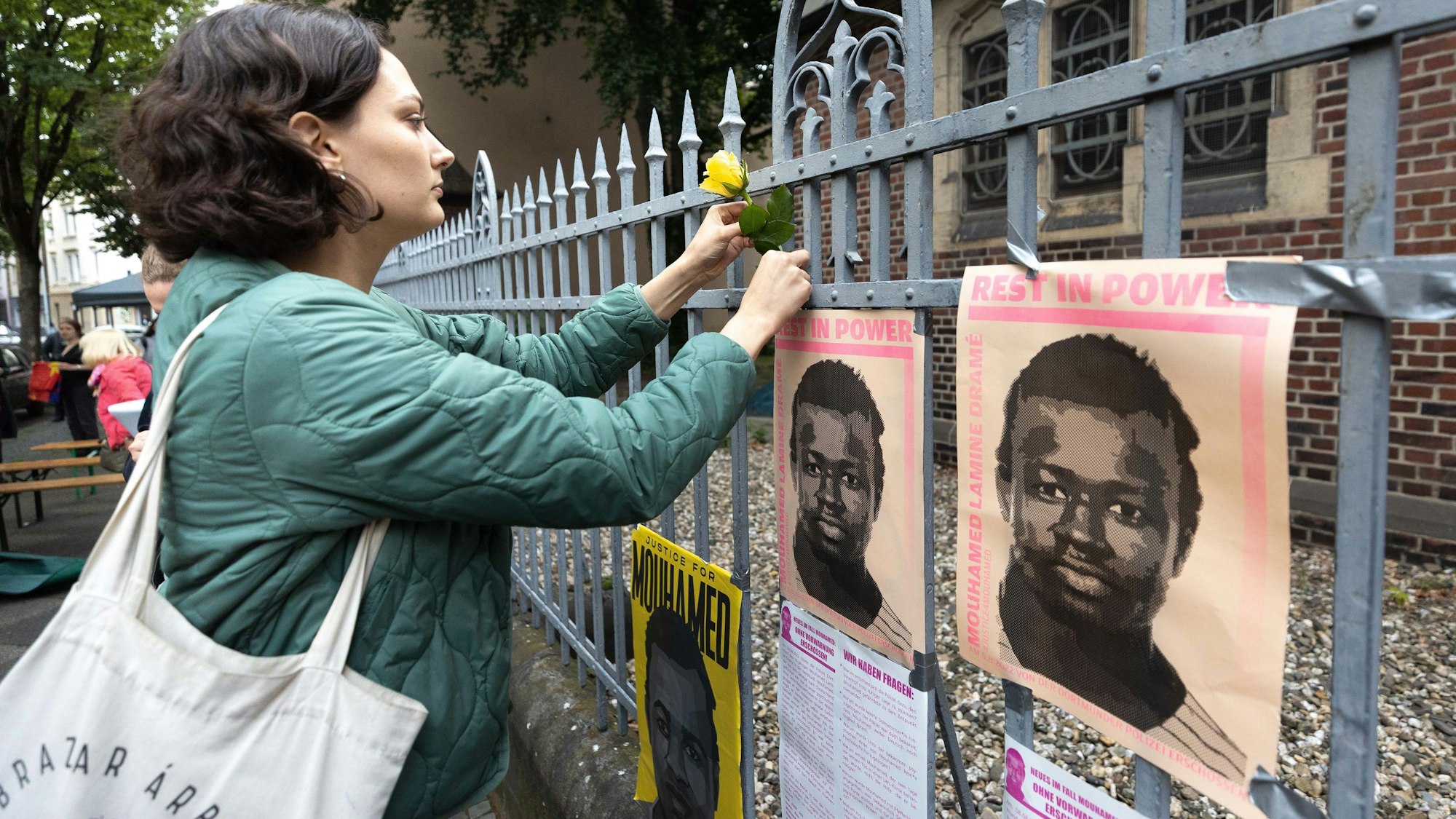 Mahnwache in Dortmund: Eine Frau erinnert mit Blumen vor Plakaten an Mouhamed Dramé.