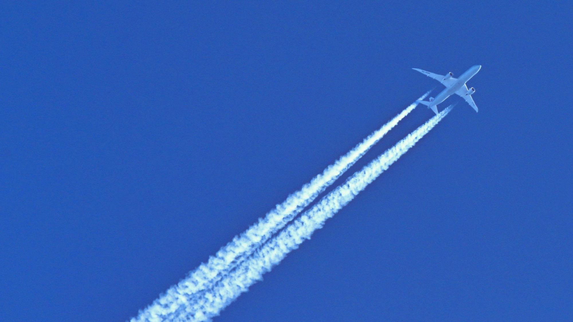 Am blauen Himmel fliegt ein Flugzeug und hinterlässt Kondensstreifen.