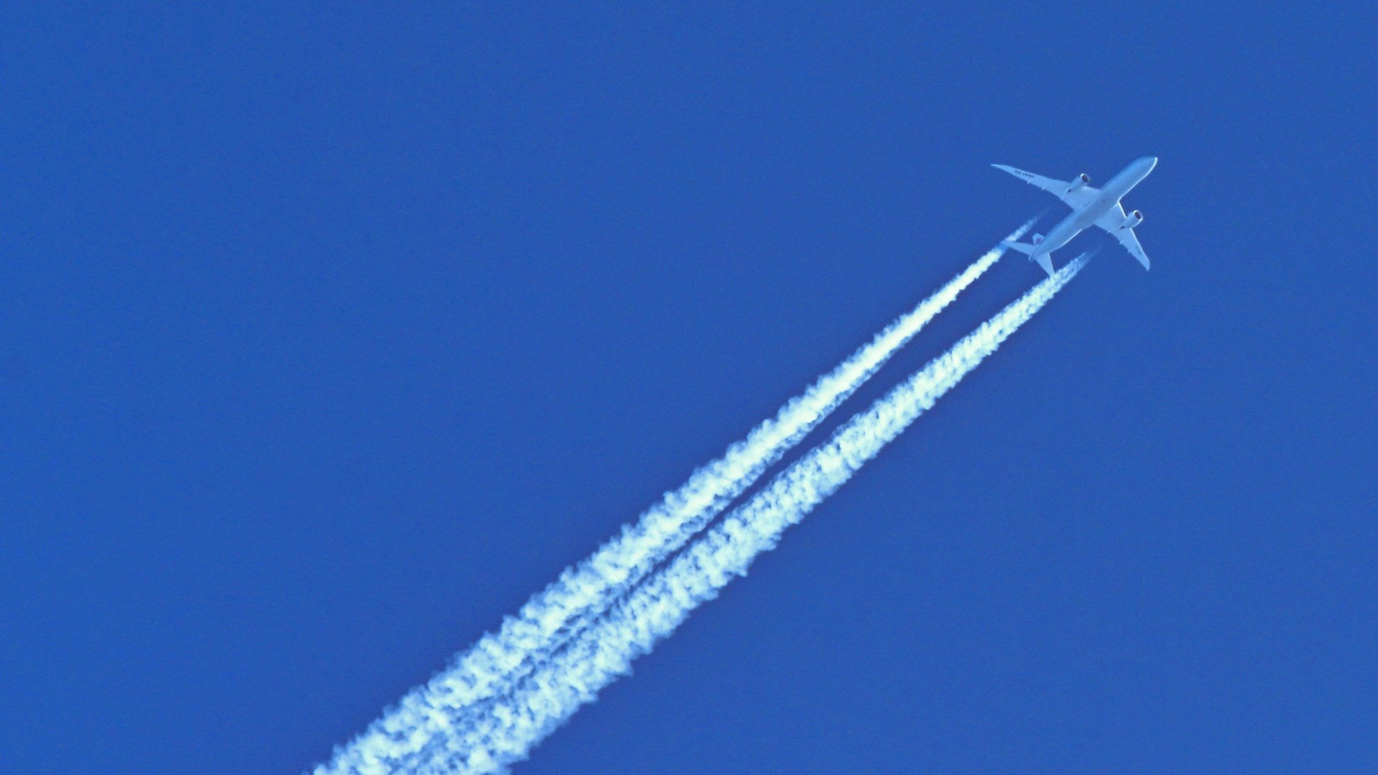 Am blauen Himmel fliegt ein Flugzeug und hinterlässt Kondensstreifen.