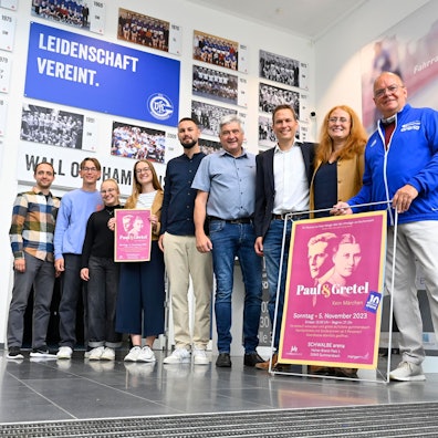 Mehrere Männer und Frauen stehen mit einem neuen Veranstaltungsprogramm in einem großen Bilderrahmen in der Halle der Schwalbe-Arena.