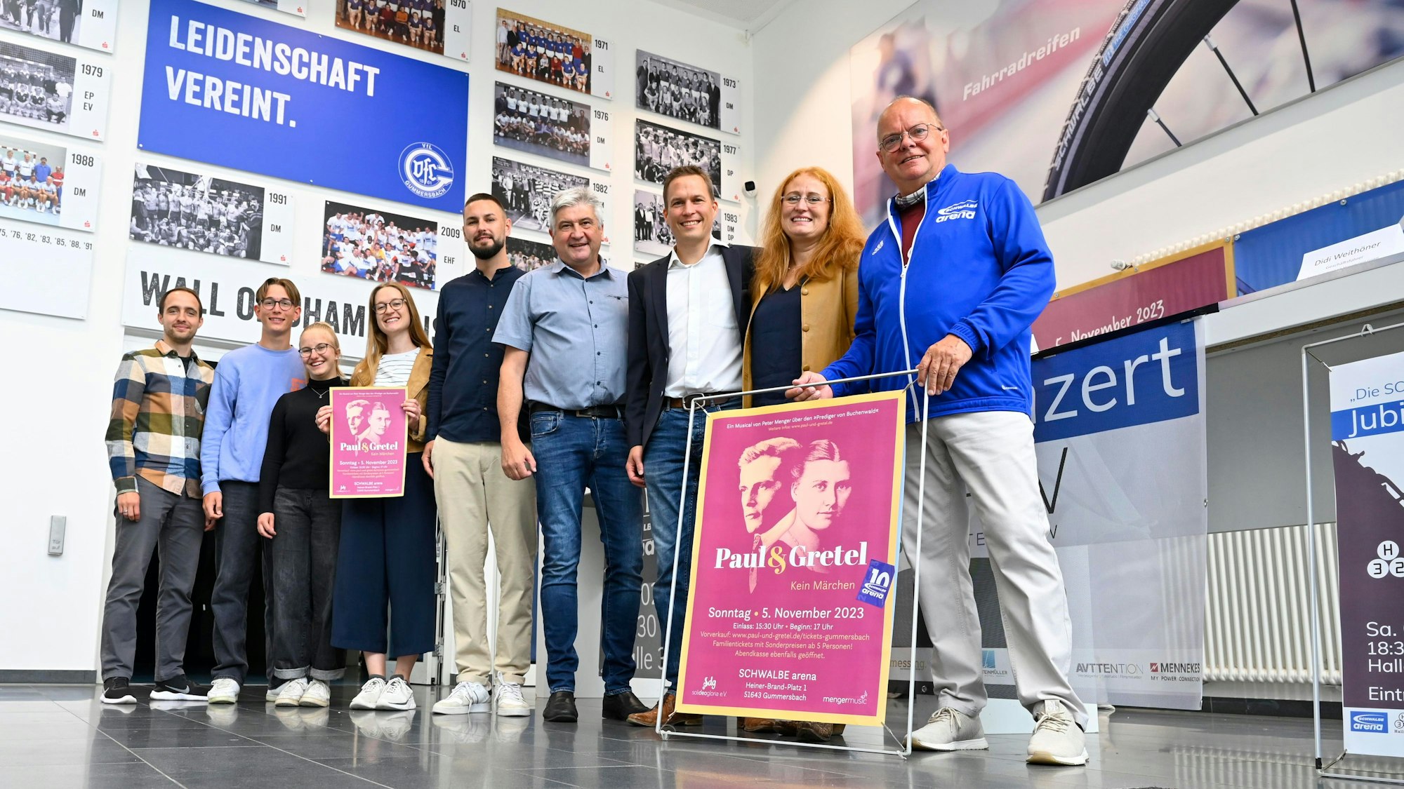 Mehrere Männer und Frauen stehen mit einem neuen Veranstaltungsprogramm in einem großen Bilderrahmen in der Halle der Schwalbe-Arena.
