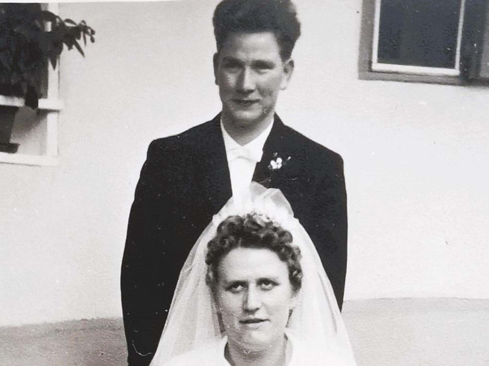 Das Paar - sie in Weiß, er im Anzug - posiert für das Hochzeitsfoto.