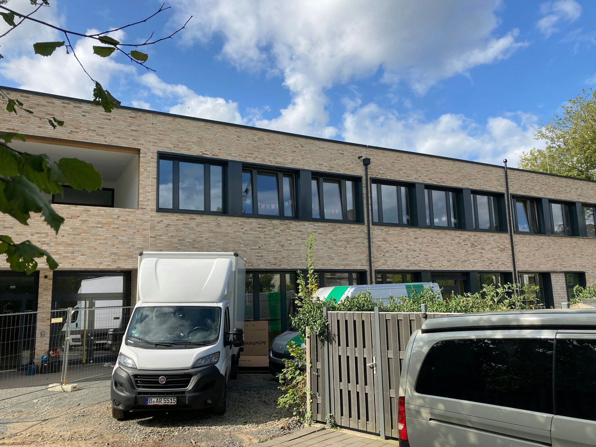 Vor einem zweistöckigen Flachdachbau parken zwei Transporter.