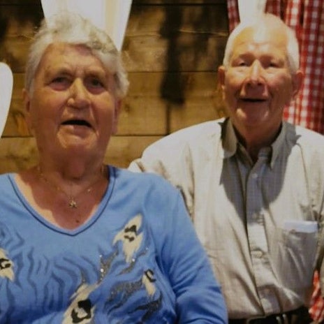 Das Paar schaut in die Kamera, die Wand hinter ihnen ist mit Herzen dekoriert.