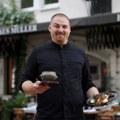 Lasse Hülsmeier steht vor dem Haus Müller und hält drei verschiedene Gerichte in der Hand
