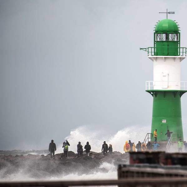 Schwerer Wellengang durch das Sturmtief „Zacharias“ an der Ostseeküste. Mehrere Schaulustige beobachten, wie die Wellen neben einem Leuchtturm bei Warnemünde an die Küste klatschen.