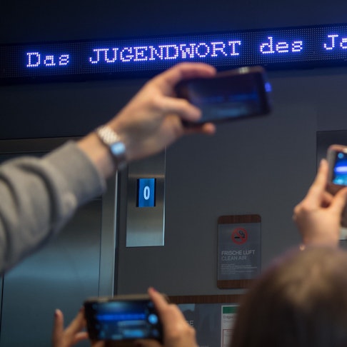 Auf einem Laufband erscheint „Jugendwort des Jahres“ über den digitalen Newsticker eines Hotels (Symbolbild).
