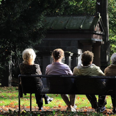 Menschen sitzen auf einer Bank auf einem Friedhof.