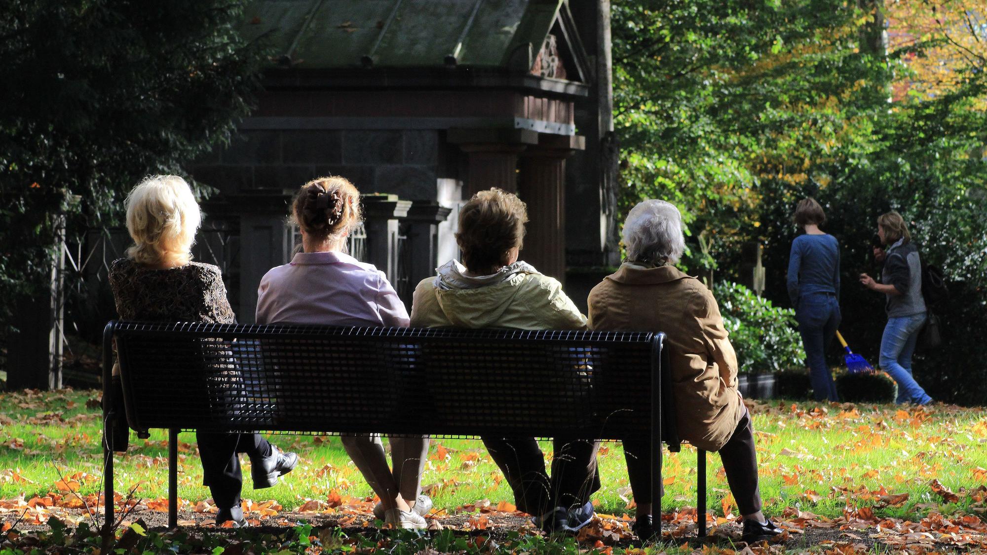 Menschen sitzen auf einer Bank auf einem Friedhof.