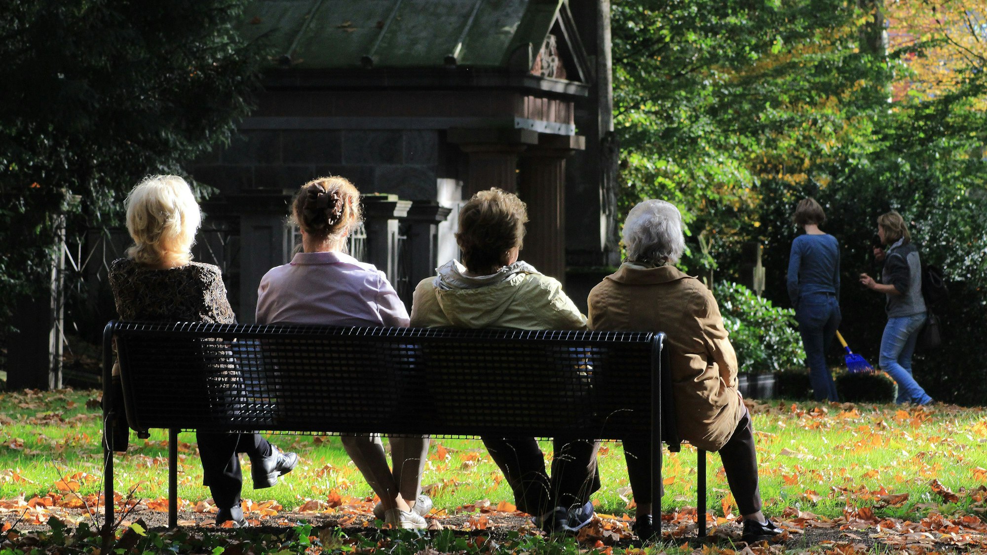 Menschen sitzen auf einer Bank auf einem Friedhof.