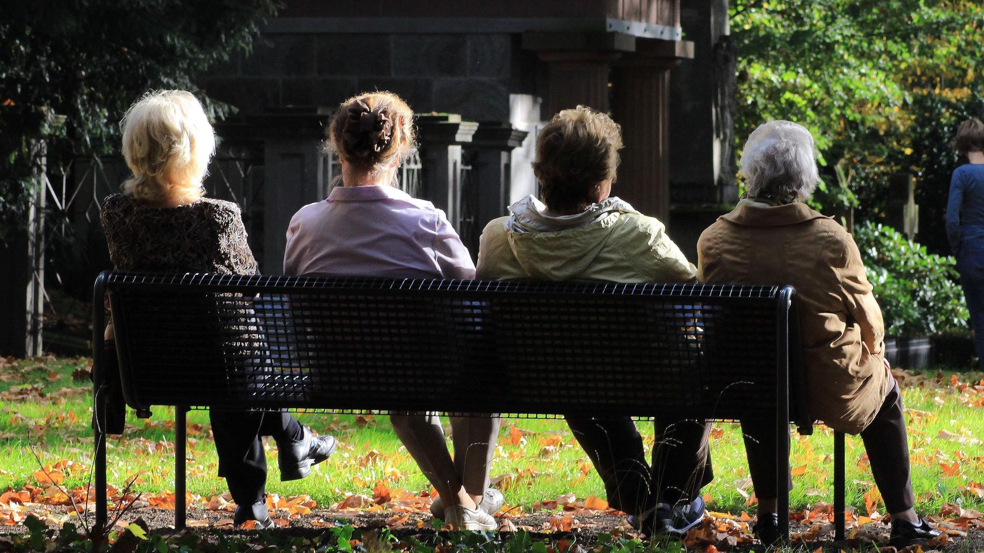 Frauen sitzen auf einer Bank auf dem Friedhof.