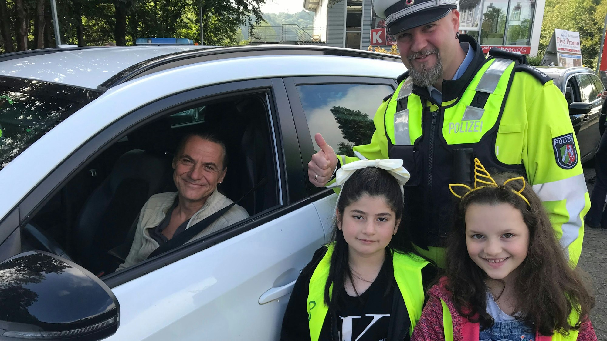 Ein Polizeibeamter in Uniform, zwei Grundschülerinnen und ein Autofahrer