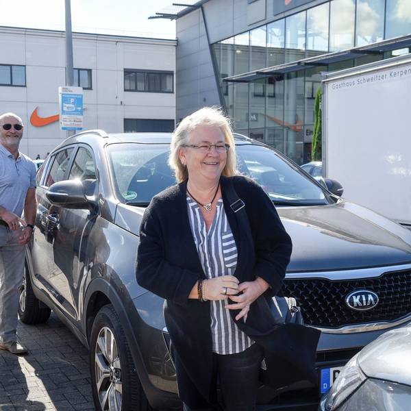 Das Bild zeigt das Ehepaar Lehnen an ihrem Auto auf dem Parkplatz des Einkaufszentrums.