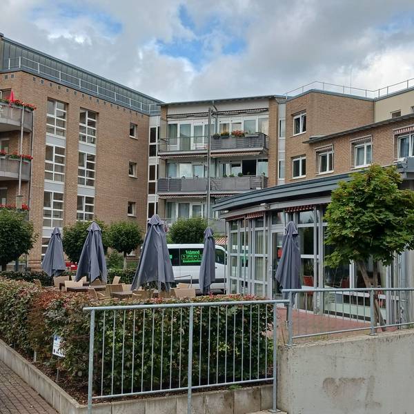 Seniorenzentrum Am Hohen Ufer in Siegburg: ein mehrstöckiges Gebäude mit Balkonen und Sonnenschirmen vor dem Eingang.