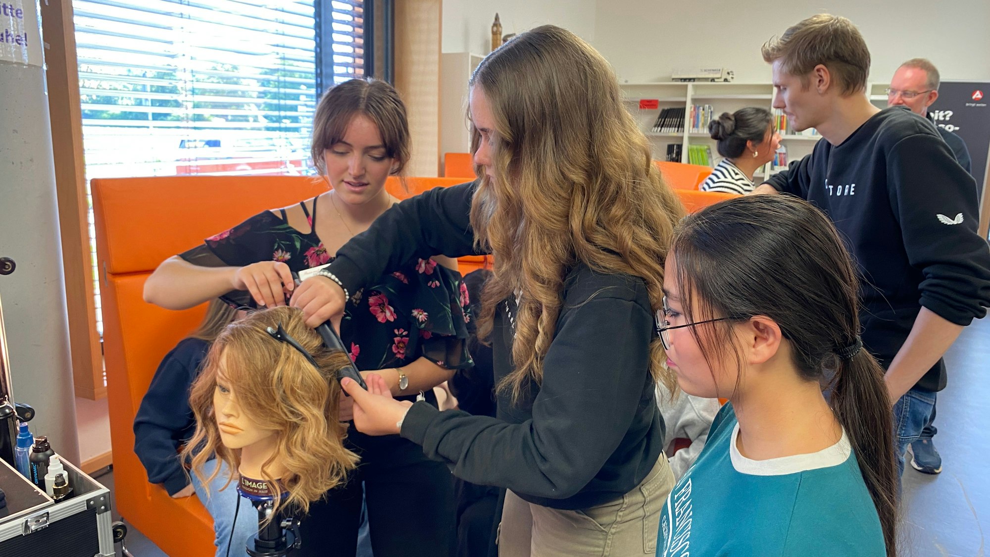 Eine Gruppe von Schülerinnen und Schülern dreht Locken an einem Kunstkopf.
